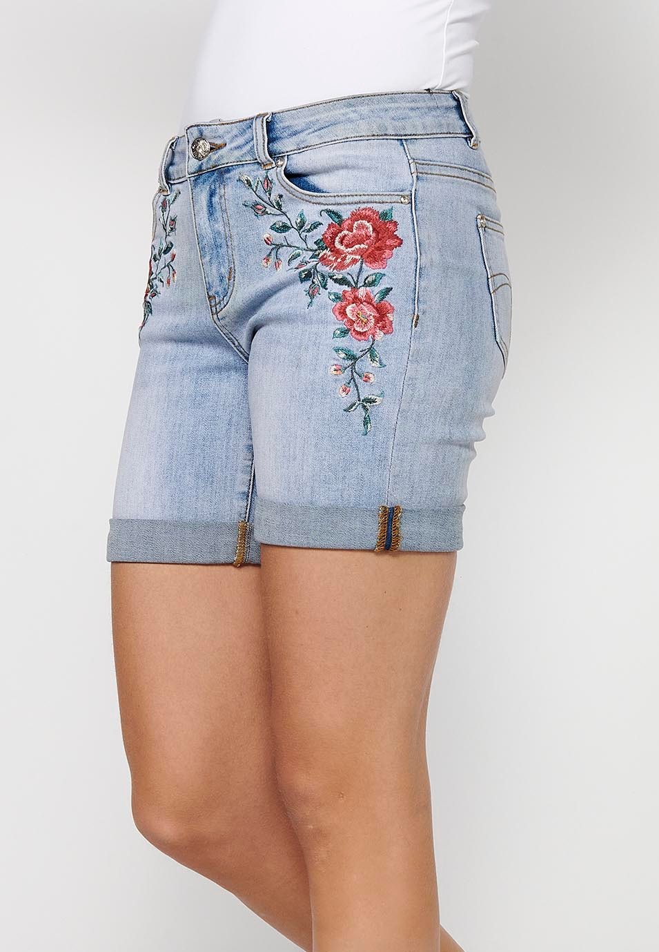 Pantalón corto short denim con cierre delantero con cremallera y botón y detalles bordados florales delanteros con cinco bolsillos, uno cerillero de color azul para mujer | Moda Actual 1