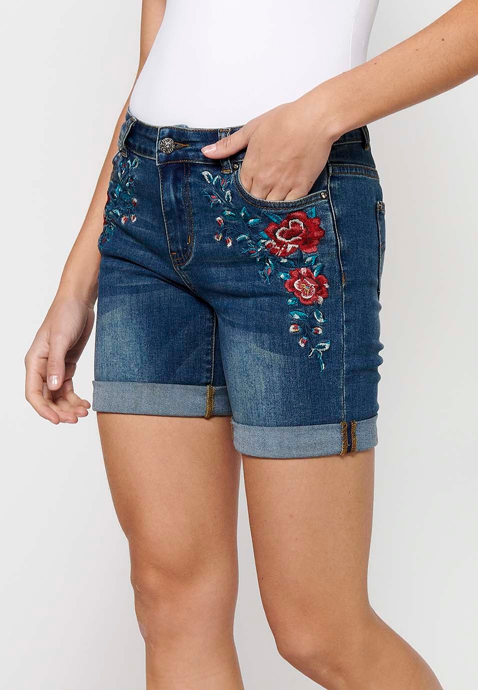 Pantalón corto short denim con cierre delantero con cremallera y botón y detalles bordados florales delanteros con cinco bolsillos, uno cerillero de color azul oscuro para mujer | Moda Actual 1