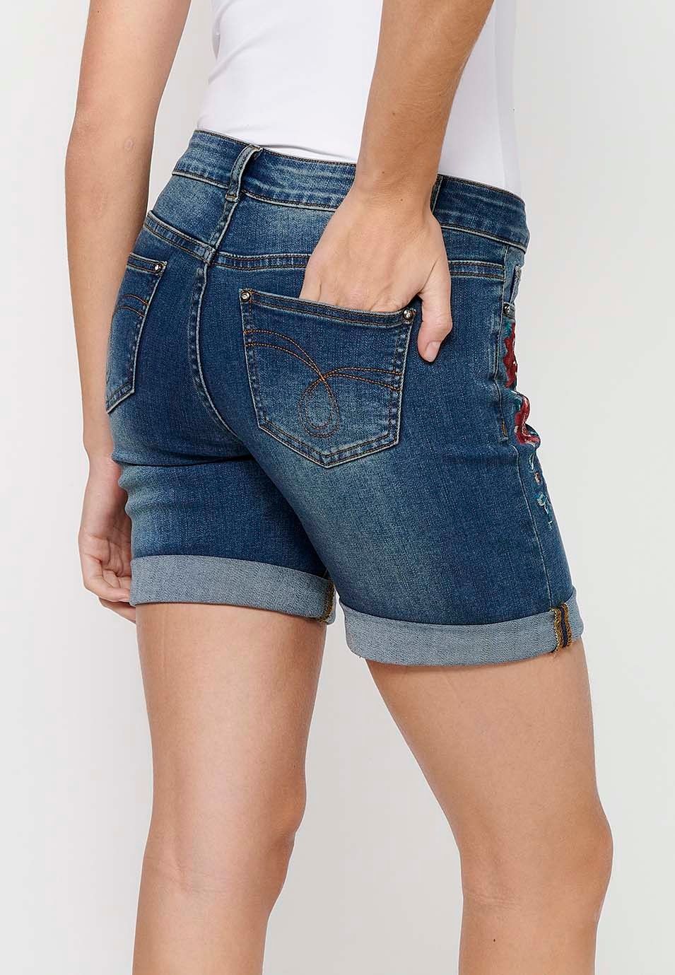 Pantalón corto short denim con cierre delantero con cremallera y botón y detalles bordados florales delanteros con cinco bolsillos, uno cerillero de color azul oscuro para mujer | Moda Actual 8