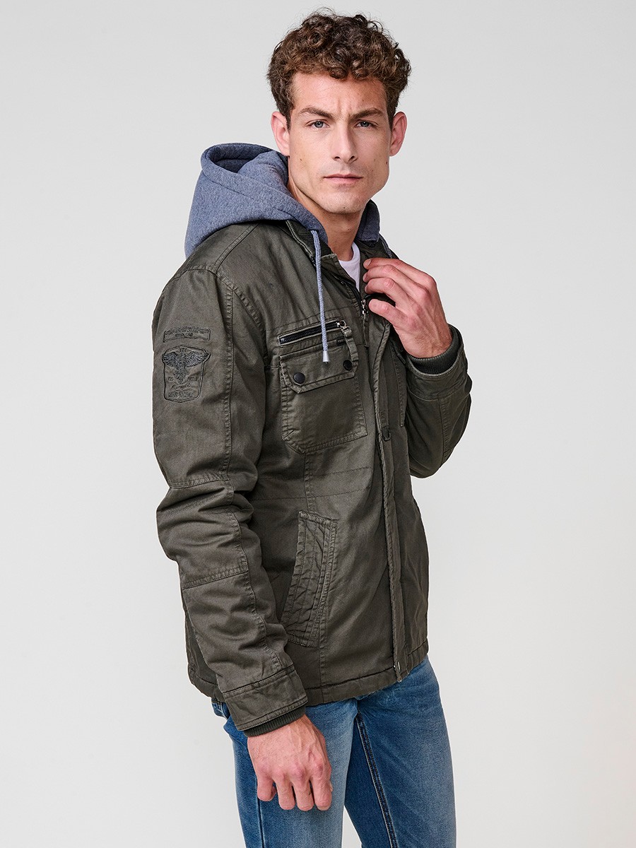 Cazadora oliva de hombre con capucha, bolsillos y cierre delantero de cremallera. Confeccionada en 100% algodón, cómoda y transpirable.