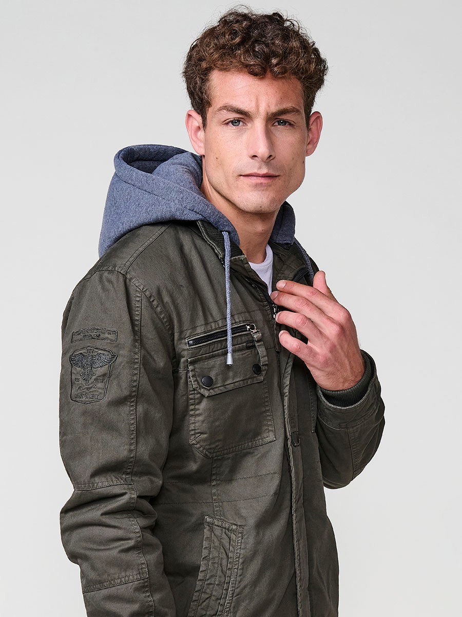 Cazadora oliva de hombre con capucha, bolsillos y cierre delantero de cremallera. Confeccionada en 100% algodón, cómoda y transpirable.