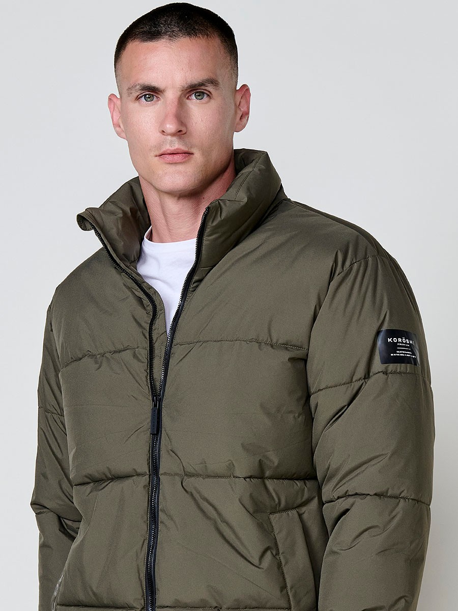 Gesteppte khakifarbene Herrenjacke mit hohem Kragen, Reißverschluss und Taschen. Aus 100 % Polyester, warm und strapazierfähig.