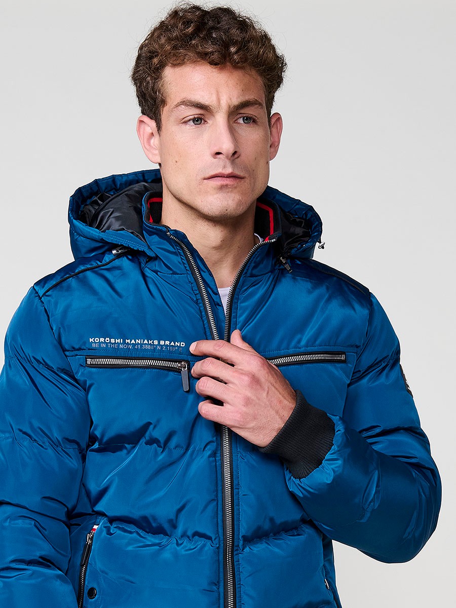 Gesteppte blaue Herrenjacke mit hohem Kragen, Kapuze, Reißverschluss und Taschen. Aus 100 % Polyester, warm und strapazierfähig.