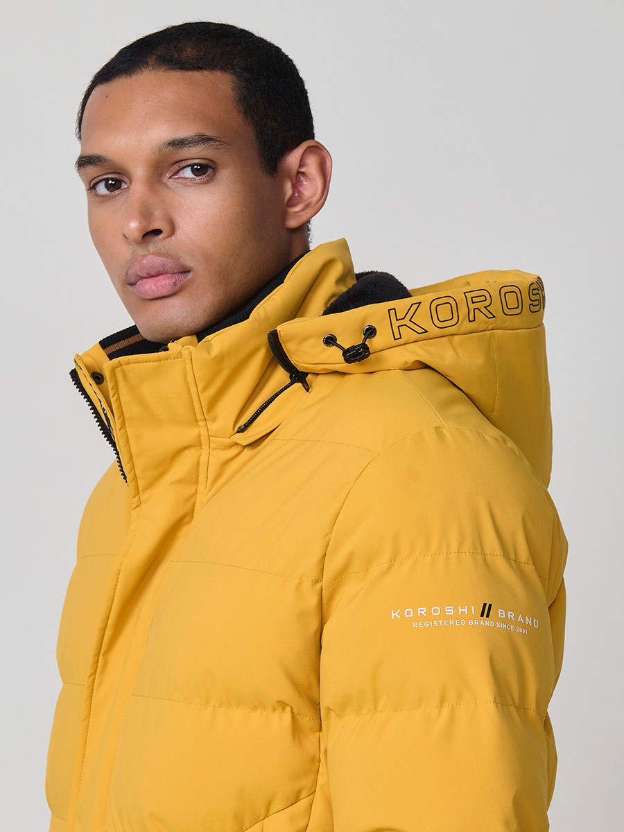 Gesteppte gelbe Herrenjacke mit hohem Kragen, Kapuze, Reißverschluss und Taschen. Aus 100 % Polyester, warm, leicht und strapazierfähig.