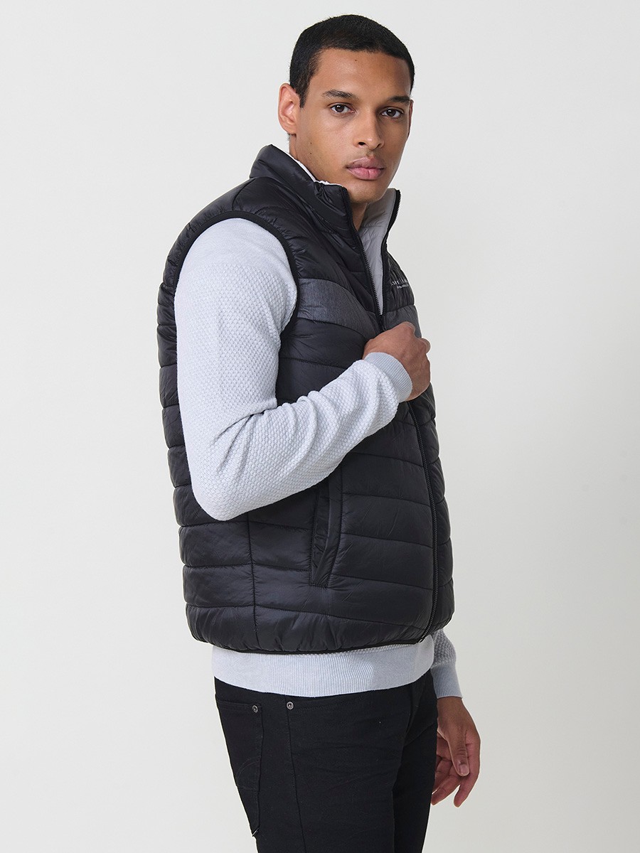Armilla encoixinada reversible d’home gris perla amb coll alt i cremallera frontal. Confeccionada en 100 % polièster, pràctica, lleugera i versàtil.