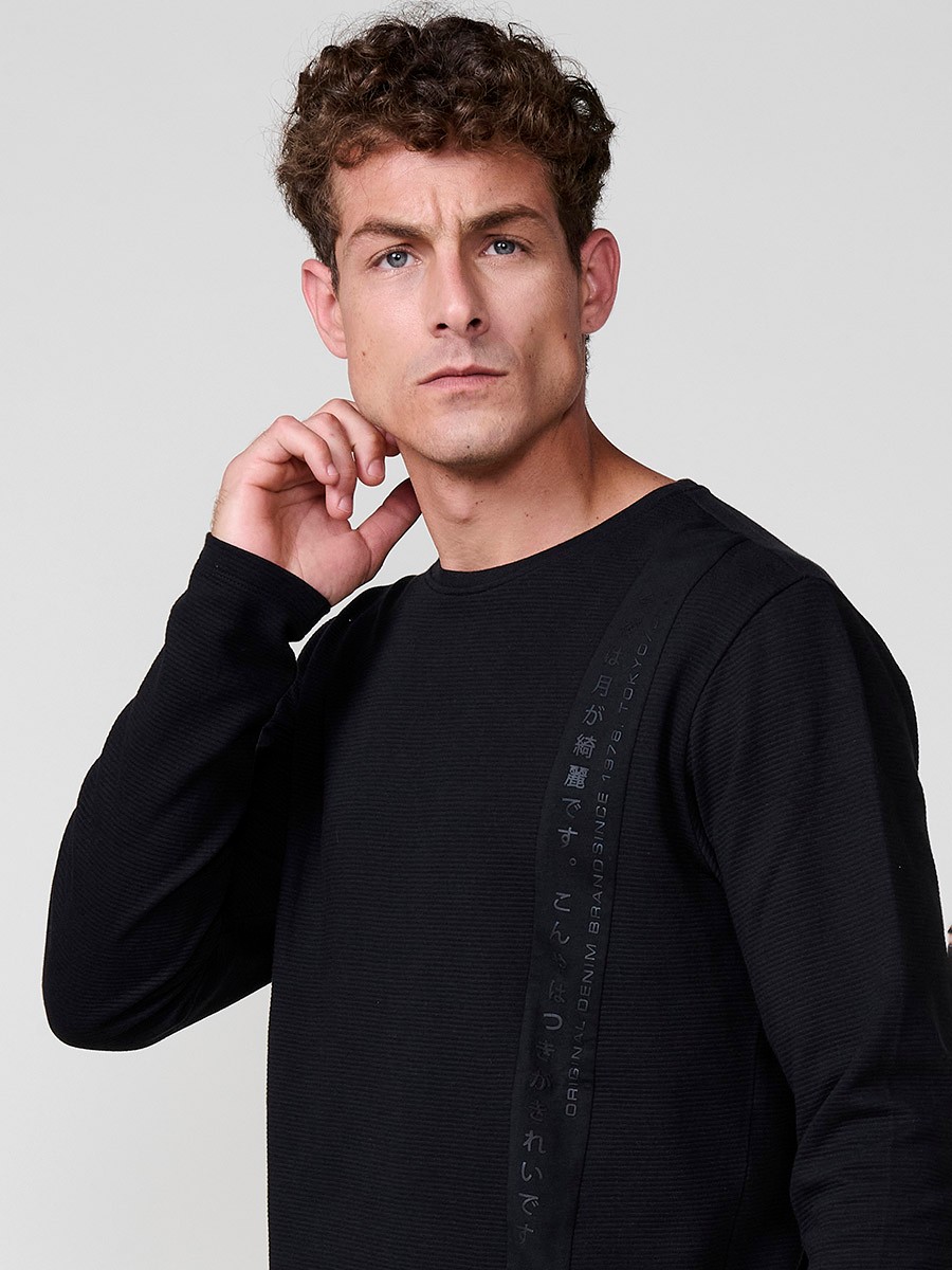 Camiseta de hombre en color negro, manga larga, cuello redondo con abertura y estampado delantero. Confeccionada en 100% algodón.