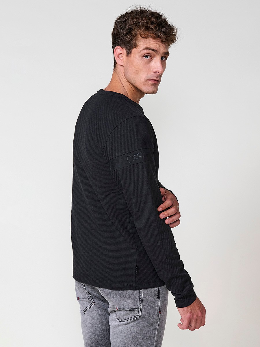 Camiseta de hombre en color negro, manga larga, cuello redondo con abertura y estampado delantero. Confeccionada en 100% algodón.