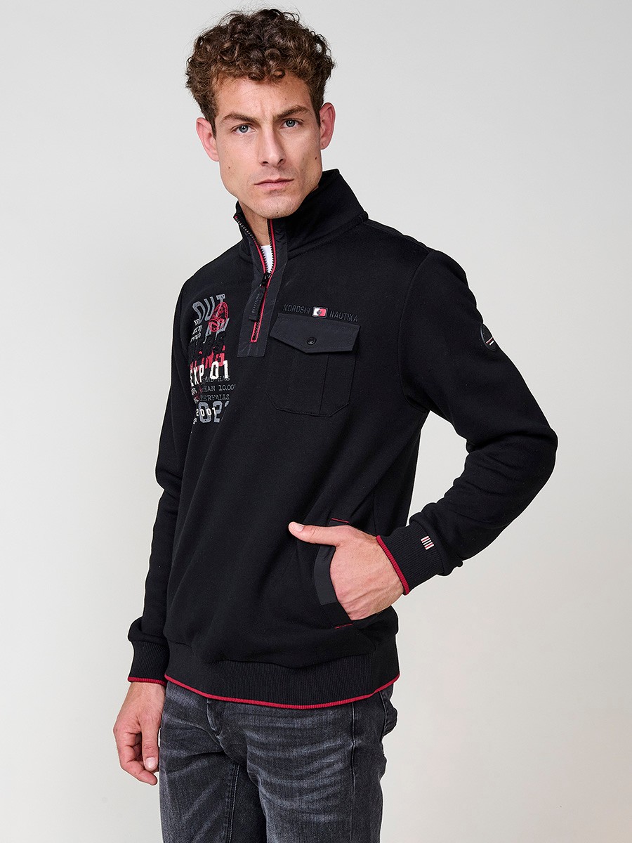 Sudadera de hombre en color negro con cuello alto y cierre de cremallera. Incluye estampado delantero, bolsillo con solapa abotonada y bolsillos laterales.