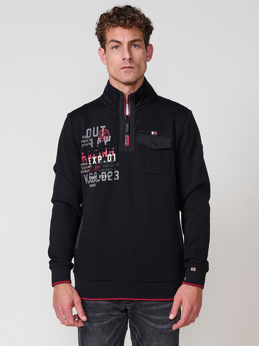 Sudadera de hombre en color negro con cuello alto y cierre de cremallera. Incluye estampado delantero, bolsillo con solapa abotonada y bolsillos laterales.