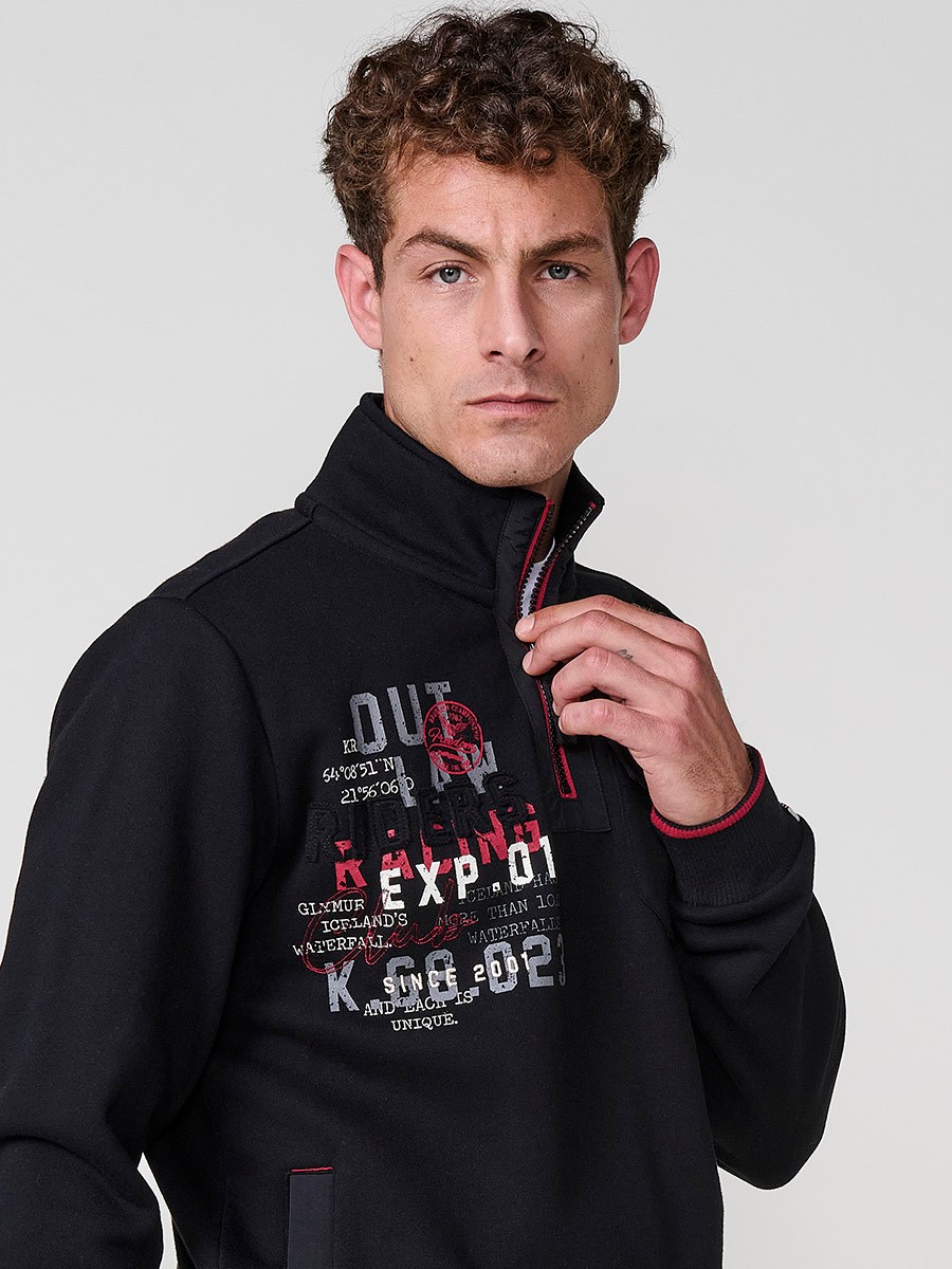 Sudadera de hombre en color negro con cuello alto y cierre de cremallera. Incluye estampado delantero, bolsillo con solapa abotonada y bolsillos laterales.