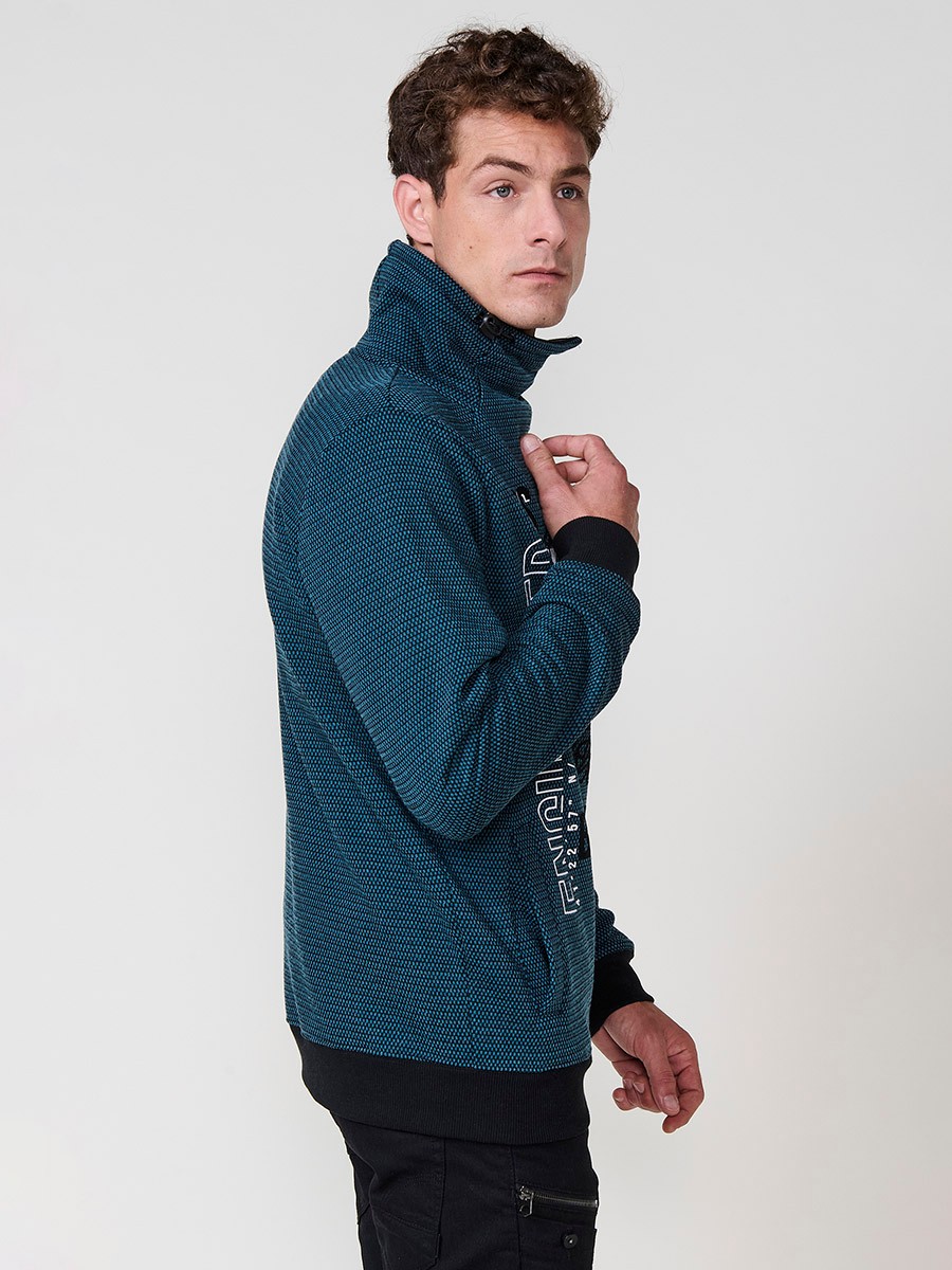 Sudadera de hombre en color petróleo con cuello alto y cremallera. Confeccionada en poliéster 100%, con estampado delantero para un estilo urbano y moderno.