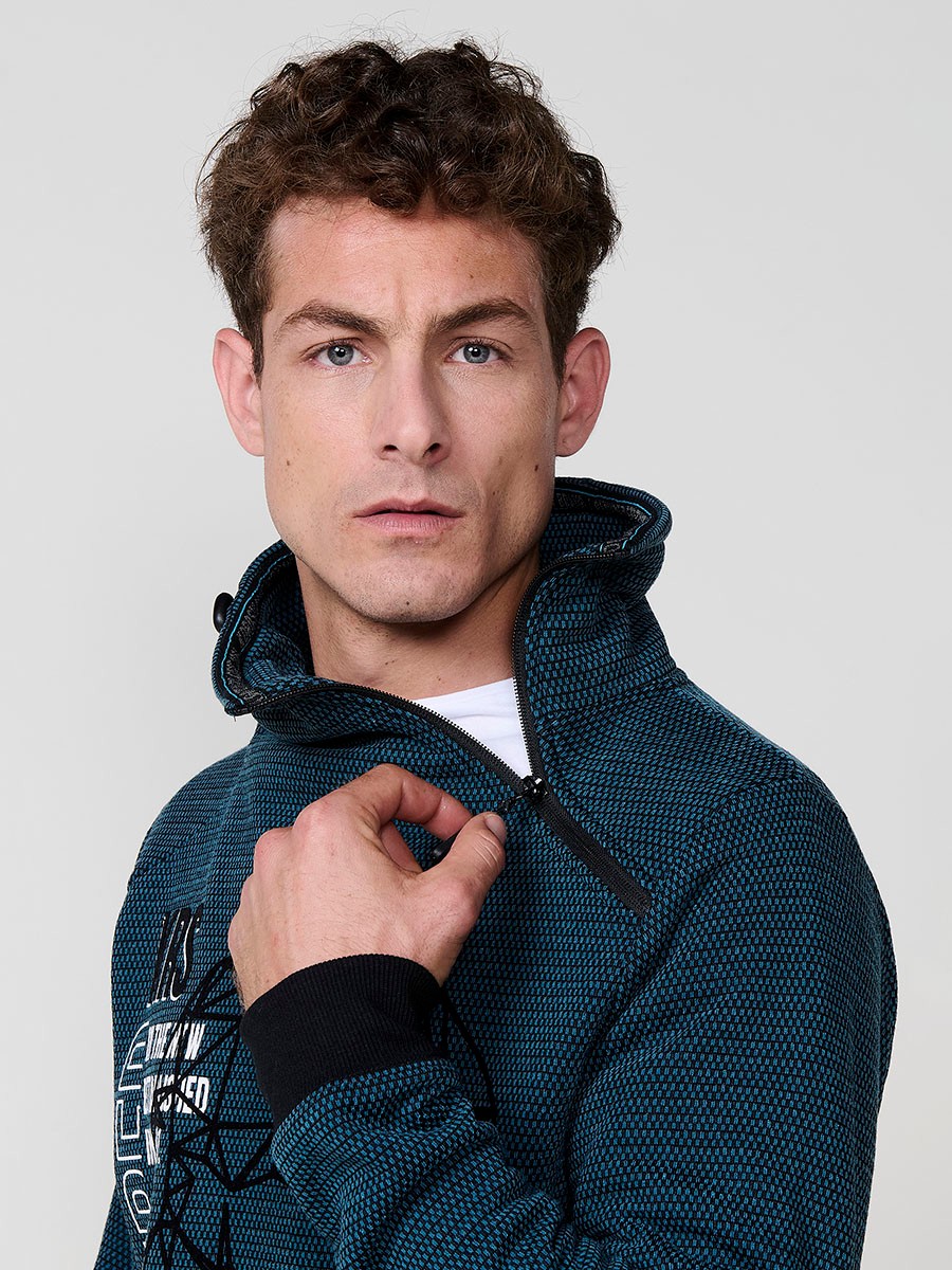 Sudadera de hombre en color petróleo con cuello alto y cremallera. Confeccionada en poliéster 100%, con estampado delantero para un estilo urbano y moderno.