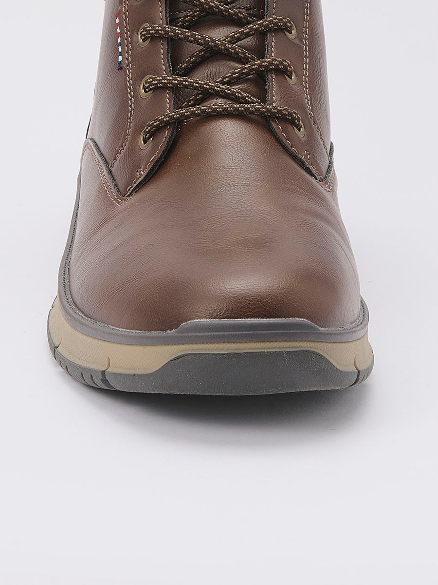 Botín de hombre en color marrón con cordones, confeccionado en poliuretano y poliéster. Diseño versátil, resistente y moderno para el día a día.