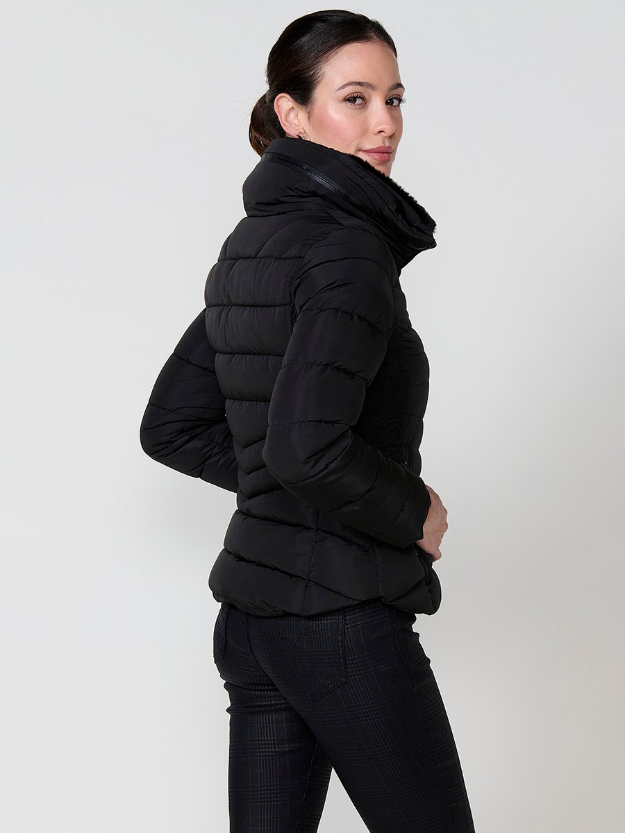 Chaqueta acolchada de mujer en color negro, cuello alto con forro efecto pelo, bolsillos laterales con cremallera y pespuntes canalé en los laterales.