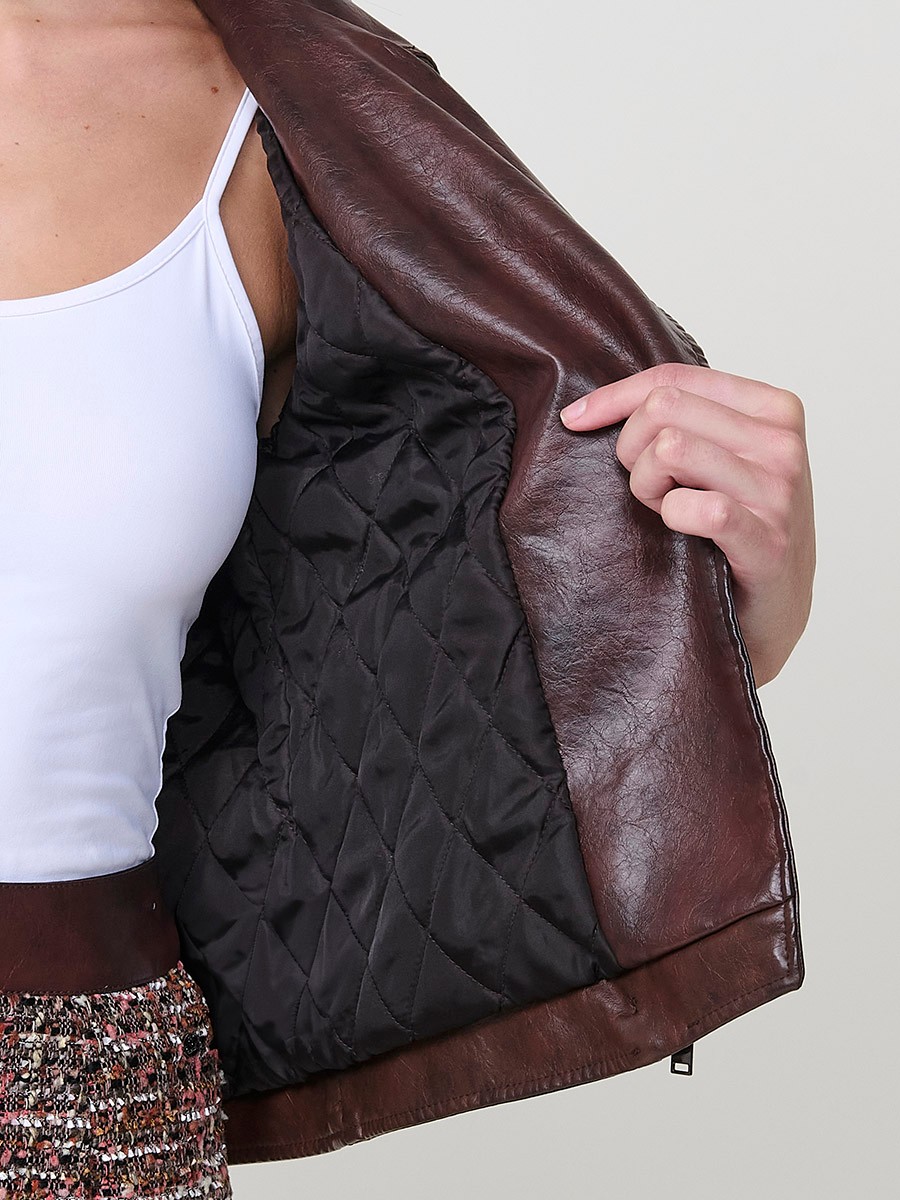 Women’s biker jacket in brown faux leather with quilted lining, metallic zipper pockets and stitched details.