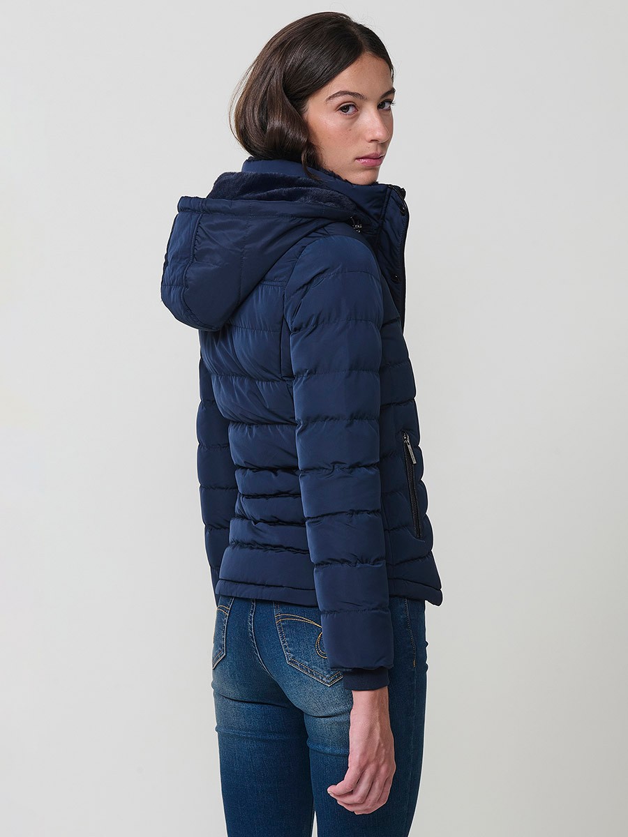 Chaqueta acolchada de mujer en color navy con cuello alto, capucha extraíble y forro efecto pelo. Prenda cálida y funcional con un estilo urbano y moderno.