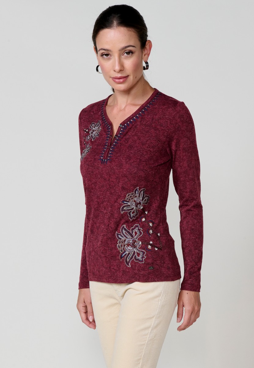 Camiseta de mujer roja de manga larga con cuello pico, tejido flamé melange, estampado floral y bordados. Detalle de tapeta con tres botones.