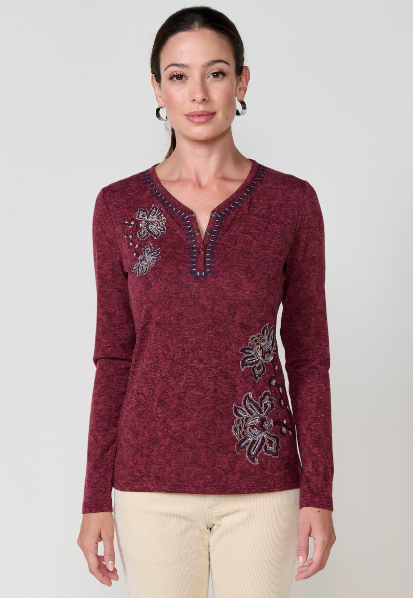Camiseta de mujer roja de manga larga con cuello pico, tejido flamé melange, estampado floral y bordados. Detalle de tapeta con tres botones.
