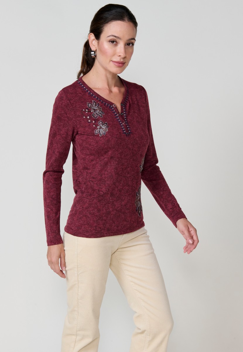 Camiseta de mujer roja de manga larga con cuello pico, tejido flamé melange, estampado floral y bordados. Detalle de tapeta con tres botones.