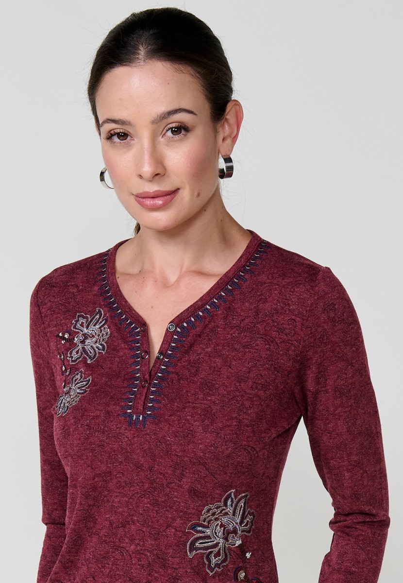 Camiseta de mujer roja de manga larga con cuello pico, tejido flamé melange, estampado floral y bordados. Detalle de tapeta con tres botones.