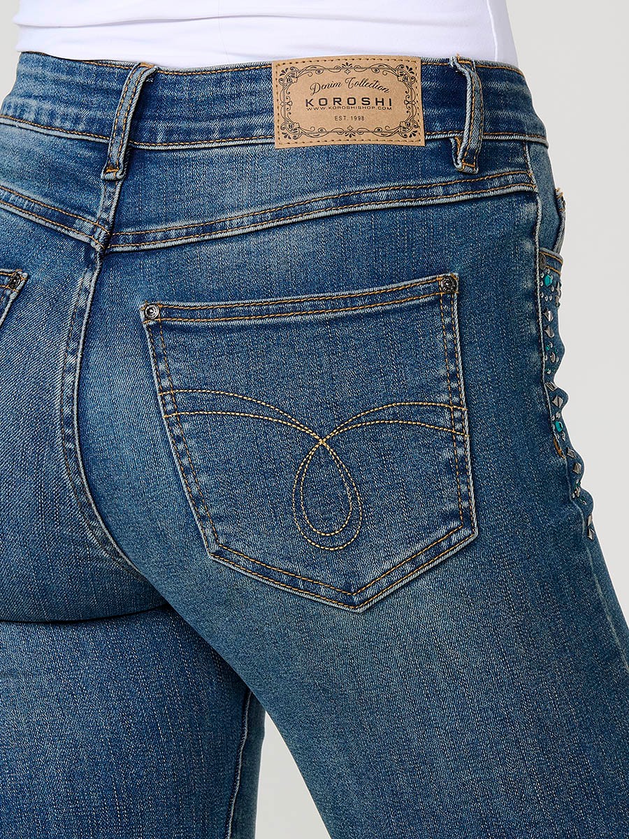 Jean femme boot cut bleu foncé stretch à taille mi-haute, cinq poches, fermeture métallique et applications de clous.