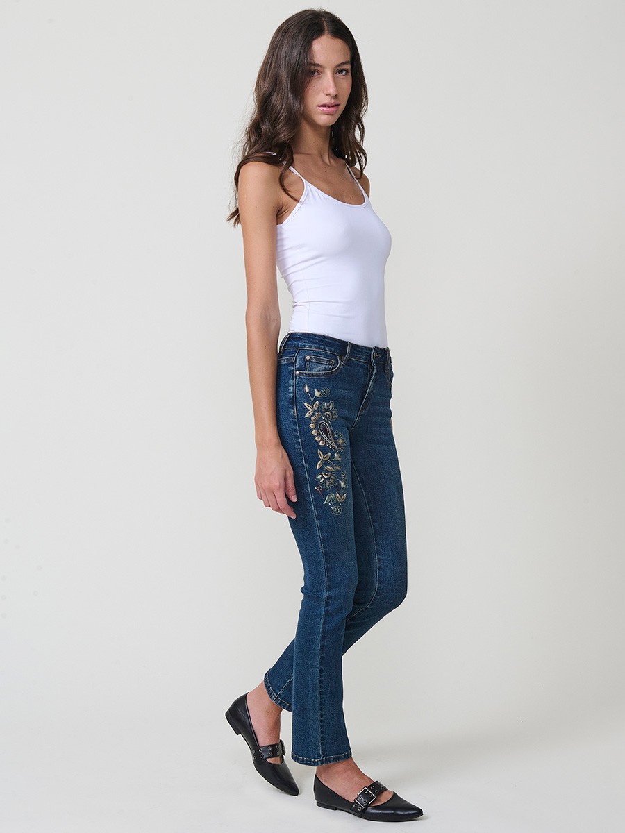Jeans slim azul muy oscuro elásticos, tiro medio, cinco bolsillos, cierre metálico y bordado con brillos en bolsillo y bajo.