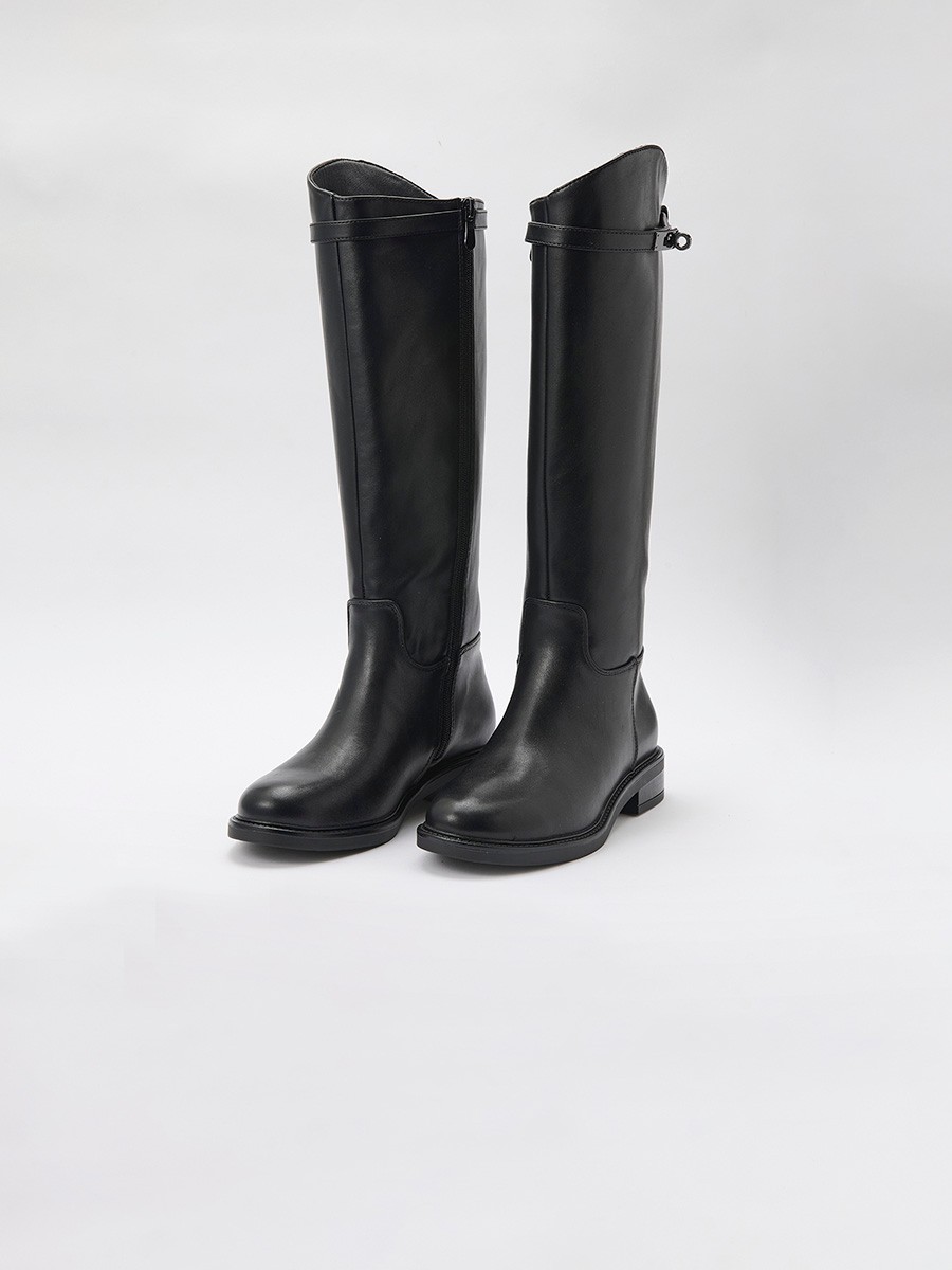 Bota plana de caña alta en efecto piel negra, estilo montar, con hebilla decorativa, cremallera interior y forro efecto pelo.