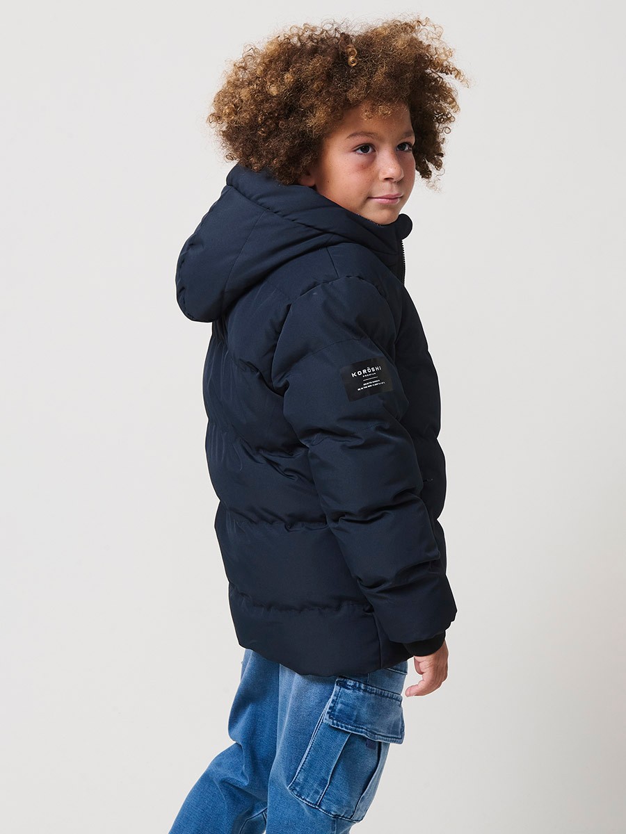Blouson matelassé garçon en coloris navy avec capuche effet fourrure et fermeture zippée. Chaud et confortable.