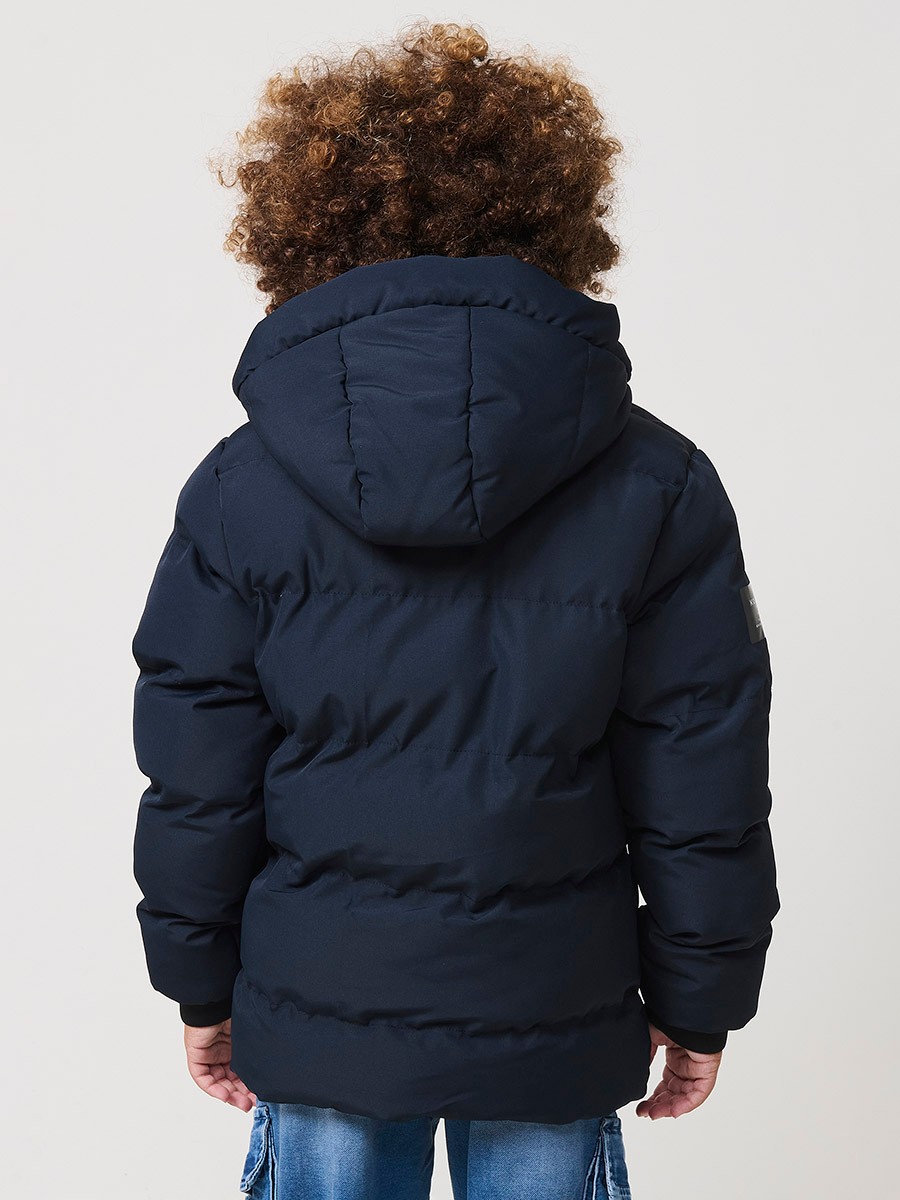Blouson matelassé garçon en coloris navy avec capuche effet fourrure et fermeture zippée. Chaud et confortable.