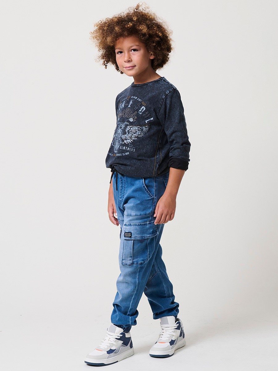 Pantalón jogger de niño en knit denim elástico color azul medio efecto lavado con bolsillos cargo. 100% algodón, cómodo y moderno.