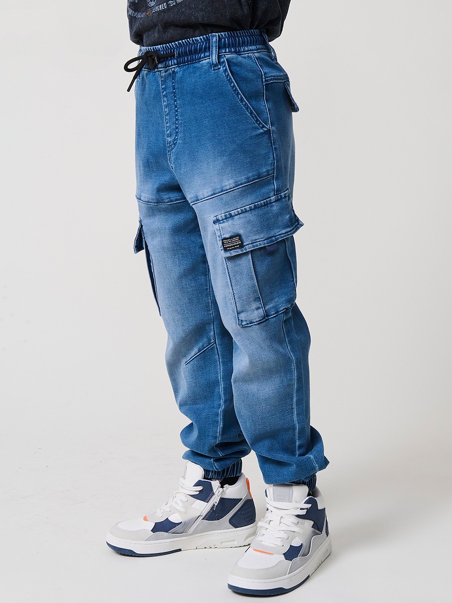 Pantalón jogger de niño en knit denim elástico color azul medio efecto lavado con bolsillos cargo. 100% algodón, cómodo y moderno.