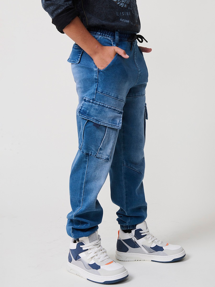 Pantalón jogger de niño en knit denim elástico color azul medio efecto lavado con bolsillos cargo. 100% algodón, cómodo y moderno.