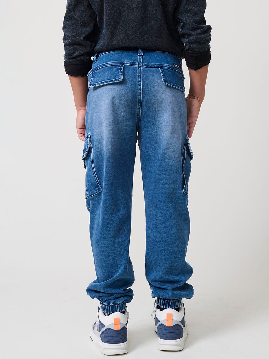 Pantalón jogger de niño en knit denim elástico color azul medio efecto lavado con bolsillos cargo. 100% algodón, cómodo y moderno.