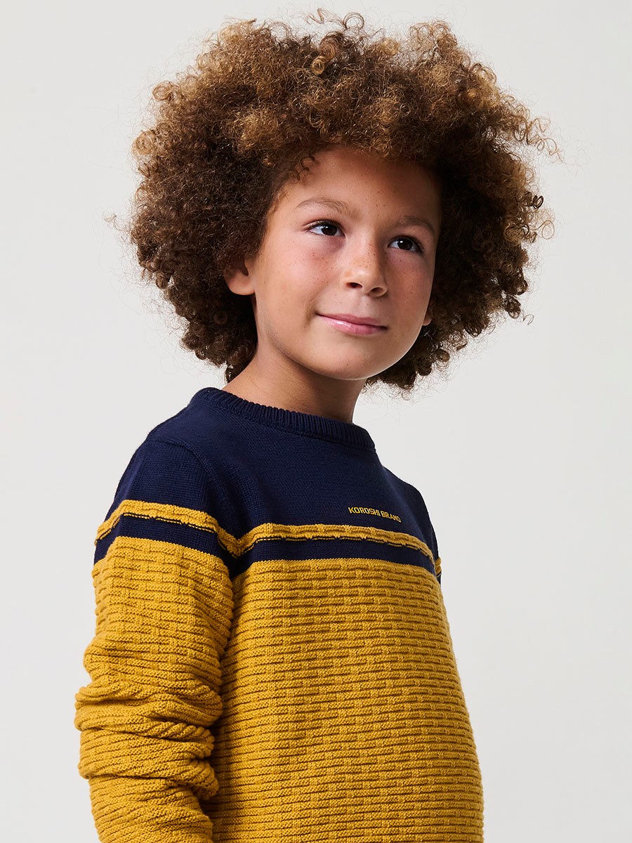 Jersey de niño en punto fantasía de algodón color mostaza con franja superior, cuello redondo y puños de canalé.