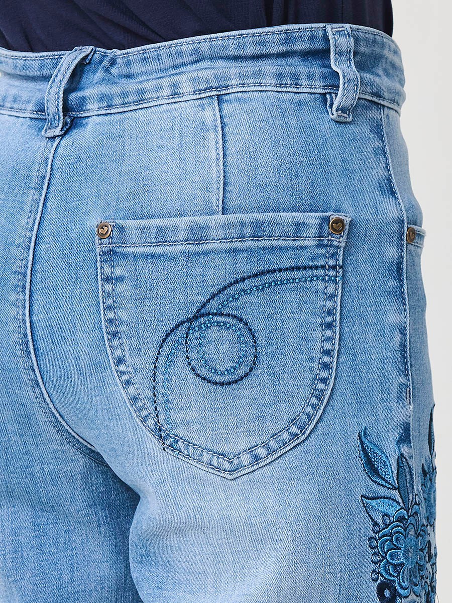 Pantalón de niña en denim elástico azul medio, pierna ancha, bajos deshilachados, cinco bolsillos y cintura regulable.