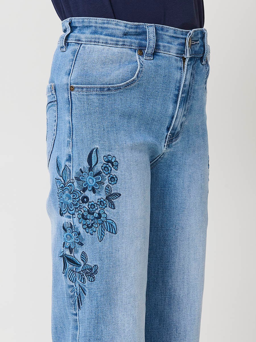 Pantalón de niña en denim elástico azul medio, pierna ancha, bajos deshilachados, cinco bolsillos y cintura regulable.