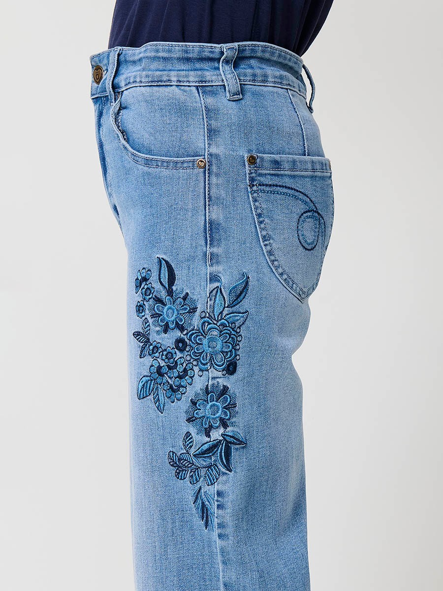 Pantalón de niña en denim elástico azul medio, pierna ancha, bajos deshilachados, cinco bolsillos y cintura regulable.