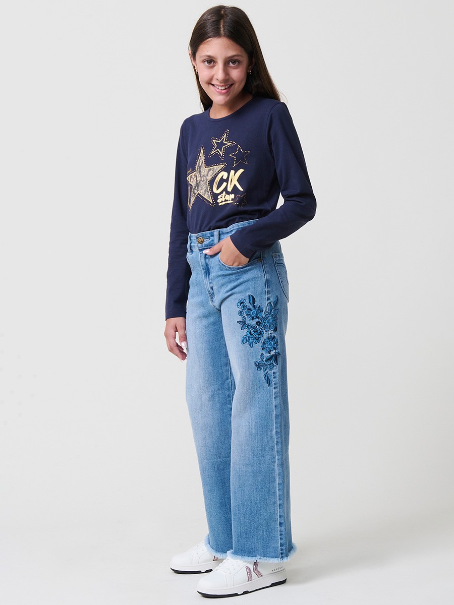 Pantalón de niña en denim elástico azul medio, pierna ancha, bajos deshilachados, cinco bolsillos y cintura regulable.