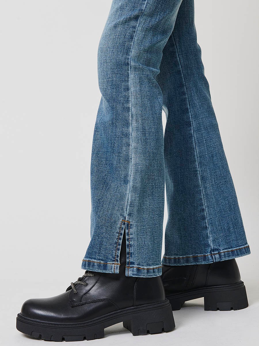 Pantalón de niña en denim elástico azul medio, pierna acampanada con cortes laterales, cinco bolsillos y cintura regulable.